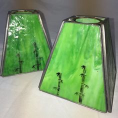 two green glass vases sitting on top of a white cloth covered tablecloth with palm trees painted on them