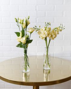 two vases filled with flowers on top of a gold table next to a white brick wall