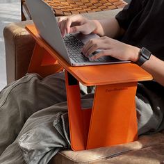 a man sitting in a chair using a laptop computer on top of an orange table