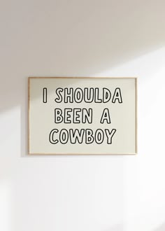 a sign that says i should be a cowboy hanging on the wall in a room