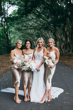 four bridesmaids pose for a photo in front of some trees and foliage at their wedding