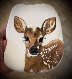 a hand holding a rock with a deer painted on it