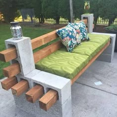 a bench made out of concrete blocks with green cushions and pillows on the seat area