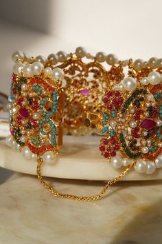 Adorn your wrist with the "Shama - Bangle," a luscious ensemble meticulously beautified by experts to infuse vibrant color into your festive attire. This exquisite bangle is embellished with the timeless beauty of multi-color stones, enhanced by a delicate addition of pearl moti, making it the perfect accessory to showcase elegance with contemporary style.The "Shama" bangle is designed with convenience in mind, featuring an openable design in the middle for easy wearing. It is a one-size-fits-mo Multicolor Fusion Gold-plated Jewelry, Multicolor Gold Plated Fusion Jewelry, Multicolor Fusion Style Gold Plated Jewelry, Multicolor Fusion Gold Plated Jewelry, Festive Gold Multi-stone Jewelry, Fusion Style Jeweled Gold Bracelets, Gold Multi-stone Fusion Jewelry, Gold Fusion Multi-stone Jewelry, Gold Multi-stone Jewelry For Celebration