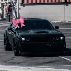 a black car with a pink bow on it's hood parked in a parking lot