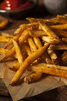 some french fries are sitting on a piece of brown paper and there is ketchup in the background