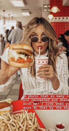 a woman holding a drink and eating a hamburger in a fast food restaurant with french fries on the side