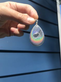 a person holding up a small pendant with a bird on it's side in front of a blue house