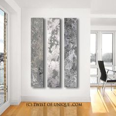 three abstract paintings on the wall in an empty room next to a table and chairs