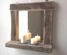 three lit candles sit on a shelf in front of a mirror that is hung on the wall