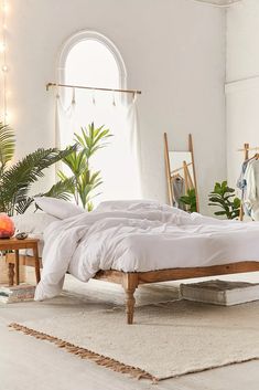 a bedroom with white linens and plants in the corner