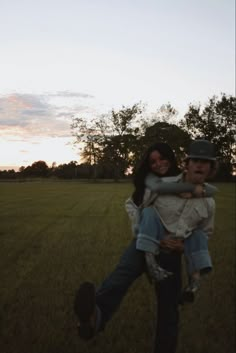 a man carrying a woman on his back in the middle of a field at sunset