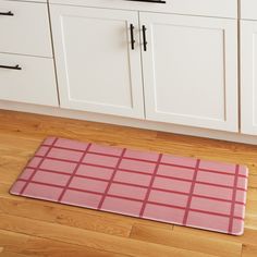 a pink mat sitting on top of a wooden floor next to white cupboards and drawers