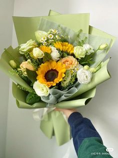 a person holding a bouquet of flowers in their hand with white, yellow and green colors