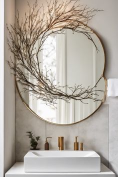 A round mirror with decorative branches above a modern bathroom sink with gold fixtures. Mirror Gallery Wall, Ornate Frames