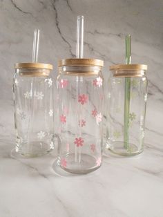 three glass jars with gold lids and flowers painted on the sides, one has a straw in it