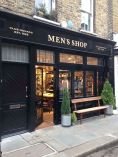 the entrance to a men's shop on a city street with benches and potted plants