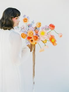 a woman holding a bouquet of flowers in her hand and looking at the sky behind her