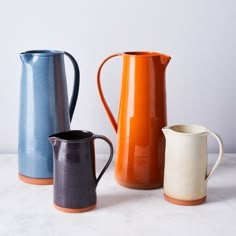 three different colored pitchers sitting next to each other on a white counter top, one is blue and the other is orange