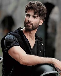 a man with a beard and black shirt on holding onto a motorcycle helmet while looking off to the side