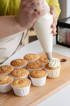 a person pouring milk into cupcakes on a cutting board with other muffins