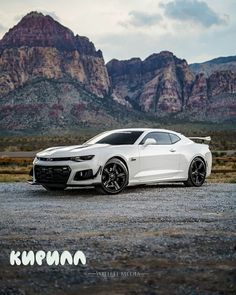 a white sports car parked in front of some mountains and rocks with the sun shining on it