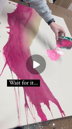 a person is painting on a large piece of paper that says wait for it with pink paint