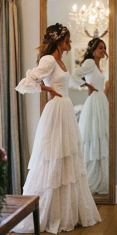 a woman standing in front of a mirror wearing a white wedding dress with ruffles