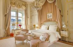 an elegant bedroom with chandelier, bed and two chairs in front of the window