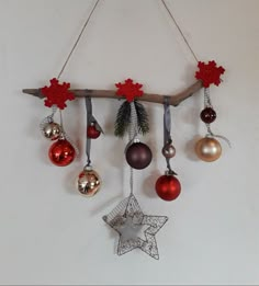 christmas ornaments hanging from a wooden branch on a white wall with red and silver baubles