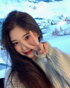 a woman with long hair posing for the camera in front of snow covered hills and mountains