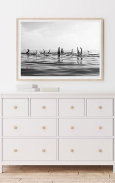 black and white photograph of surfers on surfboards in the ocean, framed above a dresser