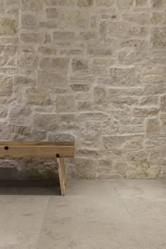 a wooden bench sitting in front of a stone wall