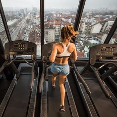 a woman running on a treadmill in a gym looking out at the city below