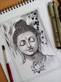 a pencil drawing of a buddha face on paper next to some pens and ink markers