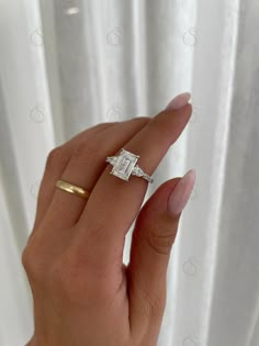 a woman's hand with a diamond ring on top of her finger and white curtains in the background