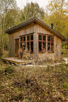 a small wooden cabin in the woods surrounded by trees and foliage, with two chairs on the deck