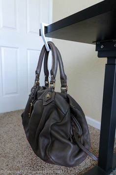 a gray purse sitting on top of a wooden table next to a black desk and white door