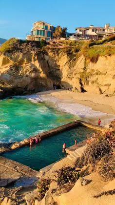 people are swimming in the ocean near some cliffs and houses on top of them with blue water