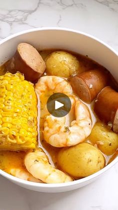 a bowl filled with shrimp, potatoes and corn on top of a white marble counter