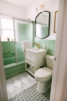 a white toilet sitting next to a bath tub under a bathroom mirror on top of a tiled floor