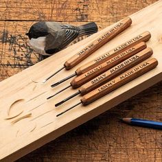 a bird sitting on top of a wooden table next to pencils