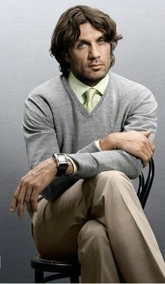 a man sitting on top of a chair wearing a sweater and tie with his arms crossed