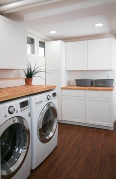 a washer and dryer in a room with white cabinets, wood floors and wooden counter tops