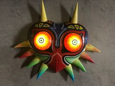 a colorful mask with horns and spikes on it's face is hanging from the wall