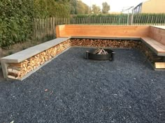 a fire pit surrounded by wooden benches and logs in a graveled area next to a fence