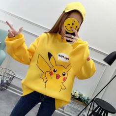 a woman wearing a yellow pokemon sweatshirt holding up her hand and making the peace sign