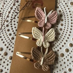 three crocheted butterfly hair clips sitting on top of a piece of brown paper