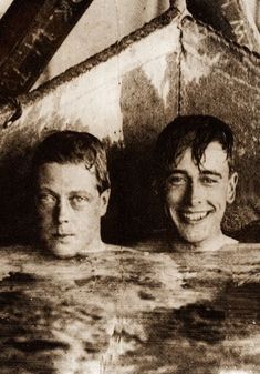 two young men are in the water with their heads above the edge of an old boat