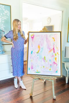 a woman standing next to a large painting on a easel in a living room